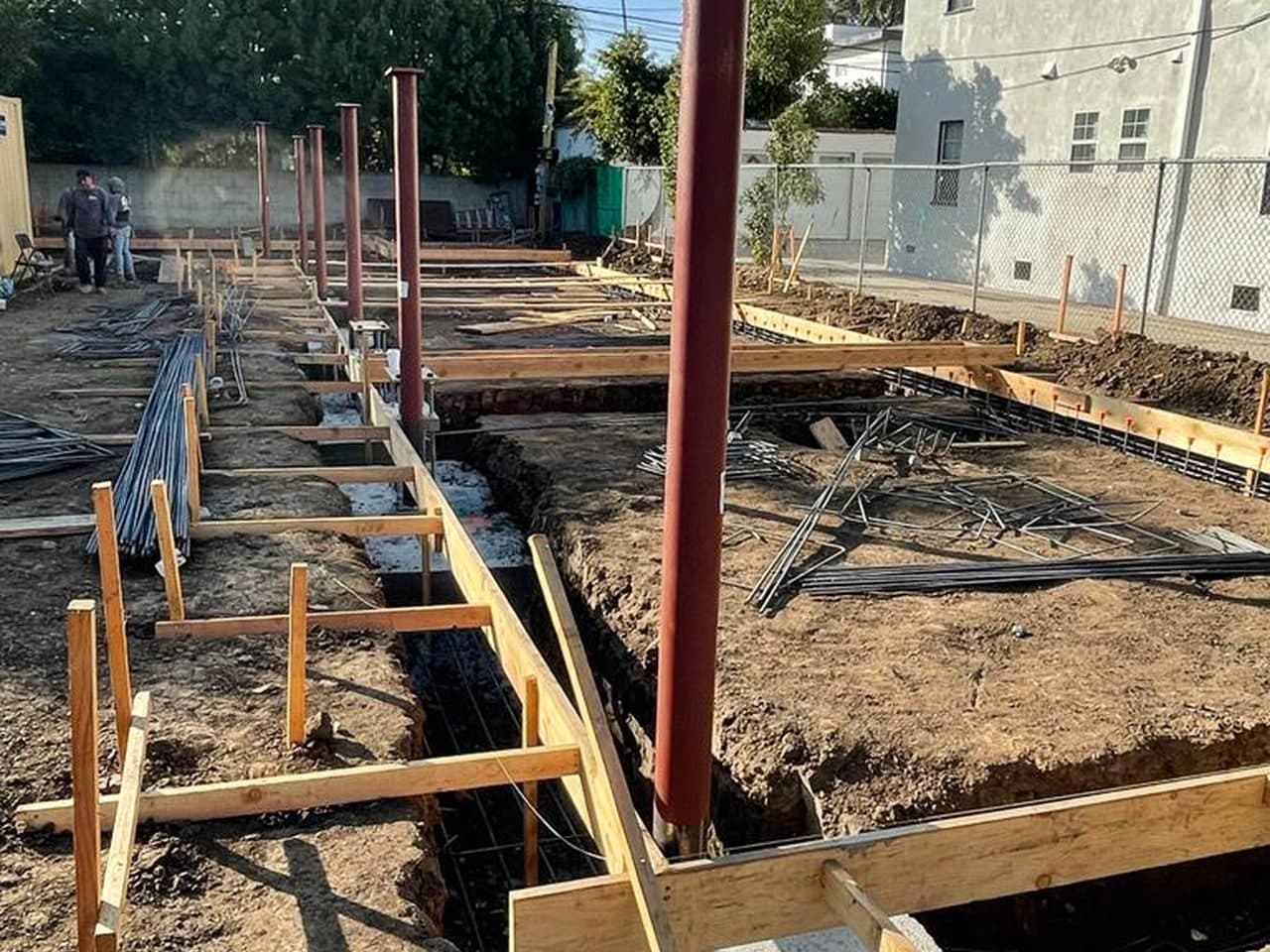 Footings, formwork, rebar, and structural steel columns set on a ground-up residential foundation.