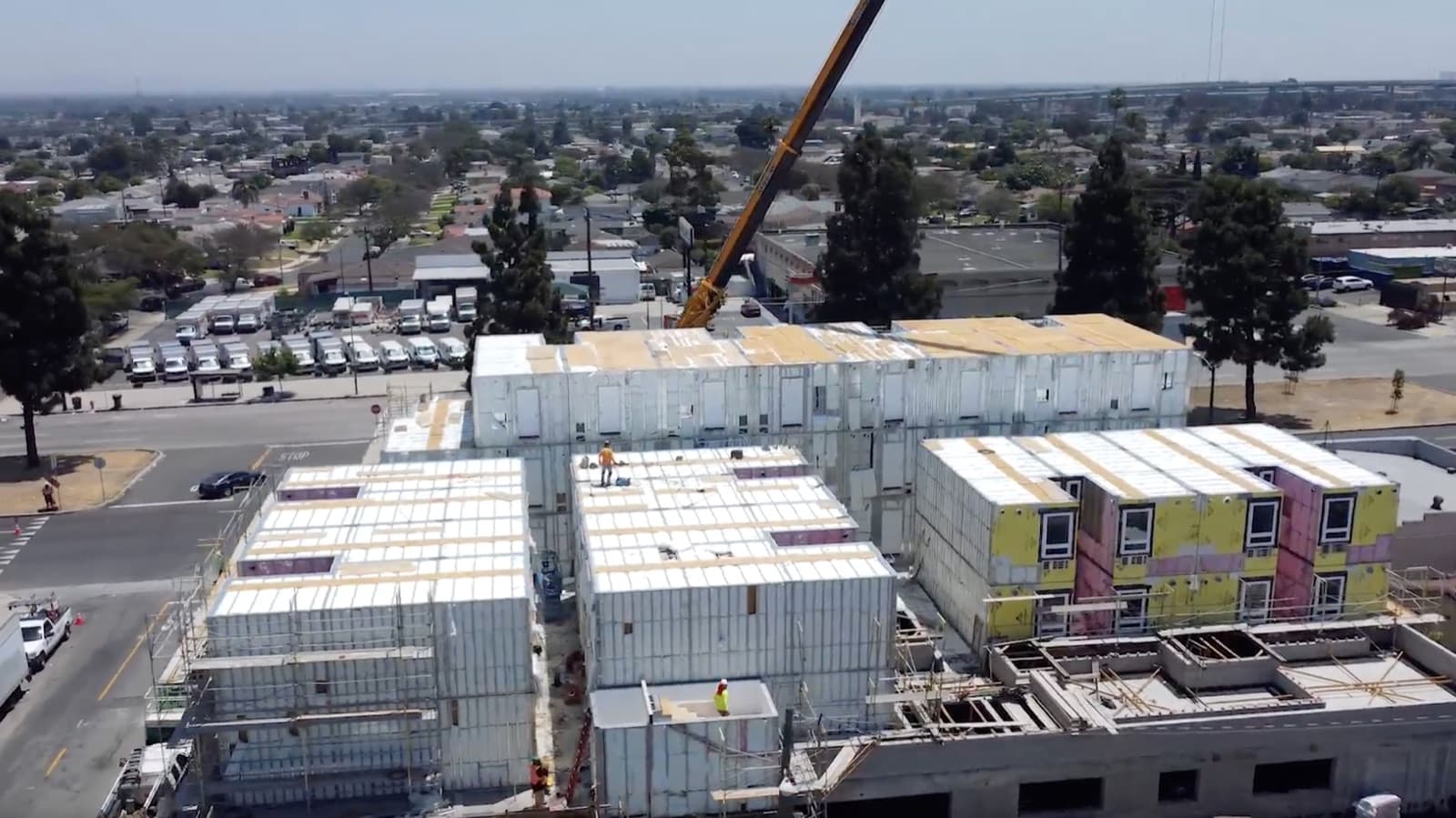 A tower crane lifting a finished volumetric module onto the multi-story building.
