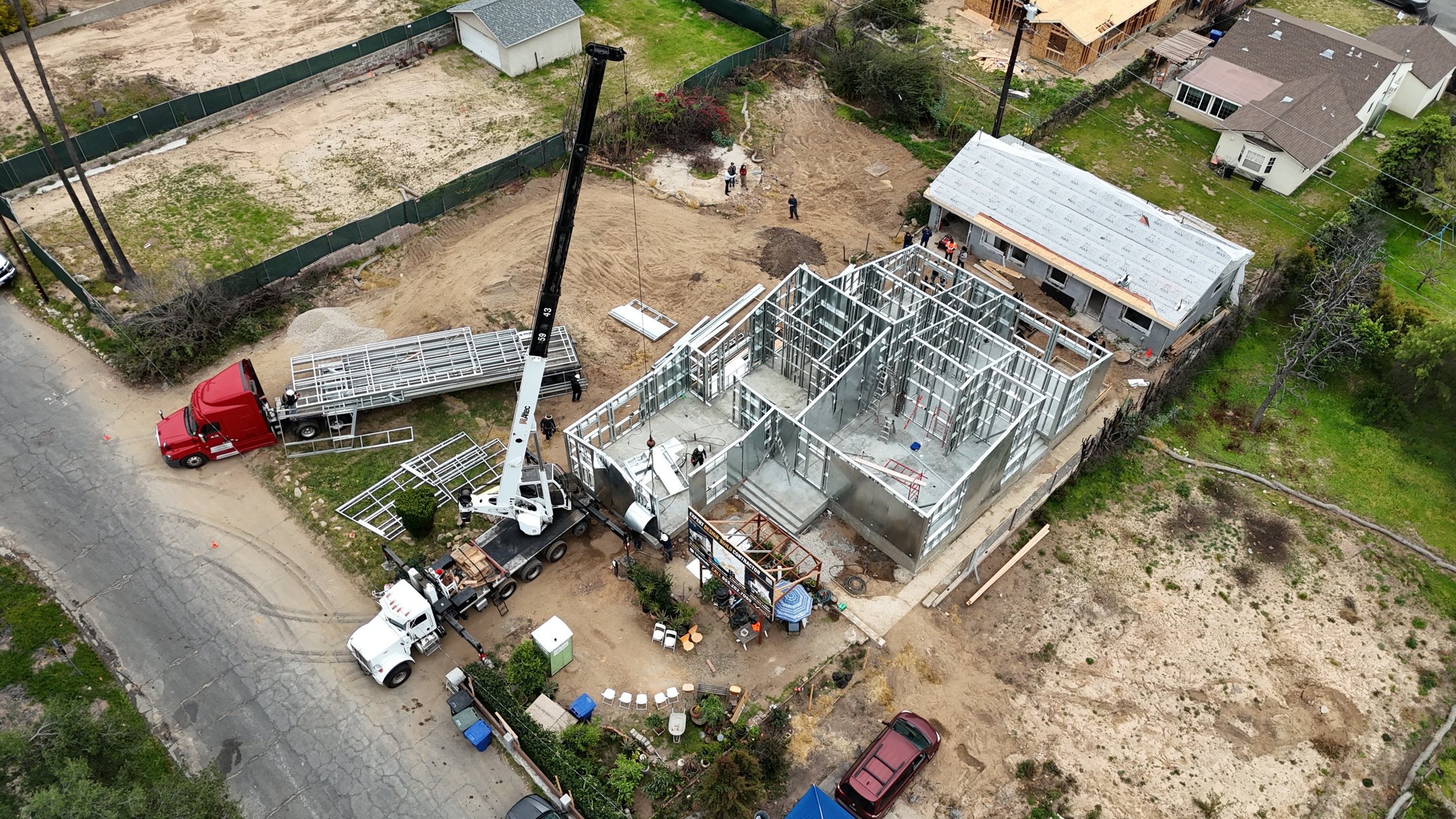 Aerial of the 480 West Palm light gauge steel rebuild in Altadena, with the delivery flatbed, crane, steel frame, and the surviving ADU.