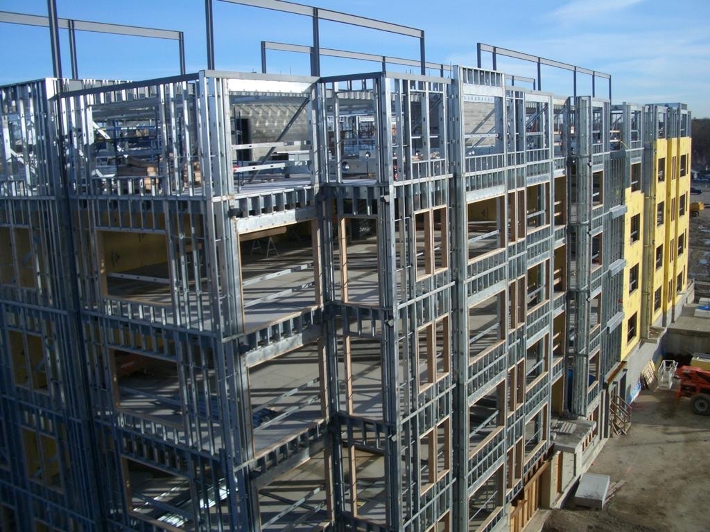 A multi-story affordable-housing building under construction, framed in light gauge steel with yellow sheathing across several floors.