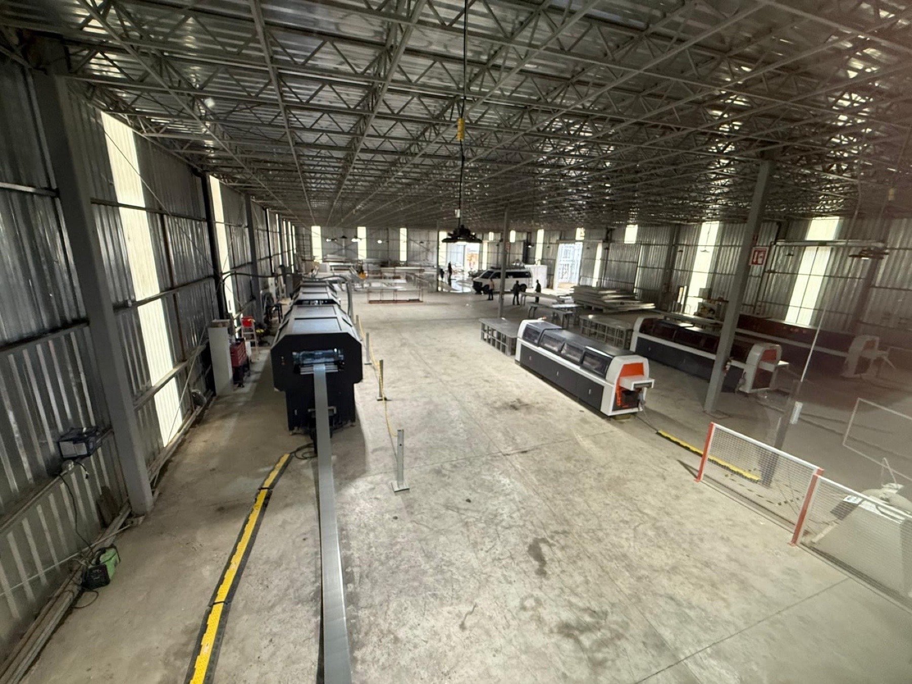 Wide view down the owned light gauge steel fabrication plant: roll-forming lines running the length of the floor under a high trussed roof.