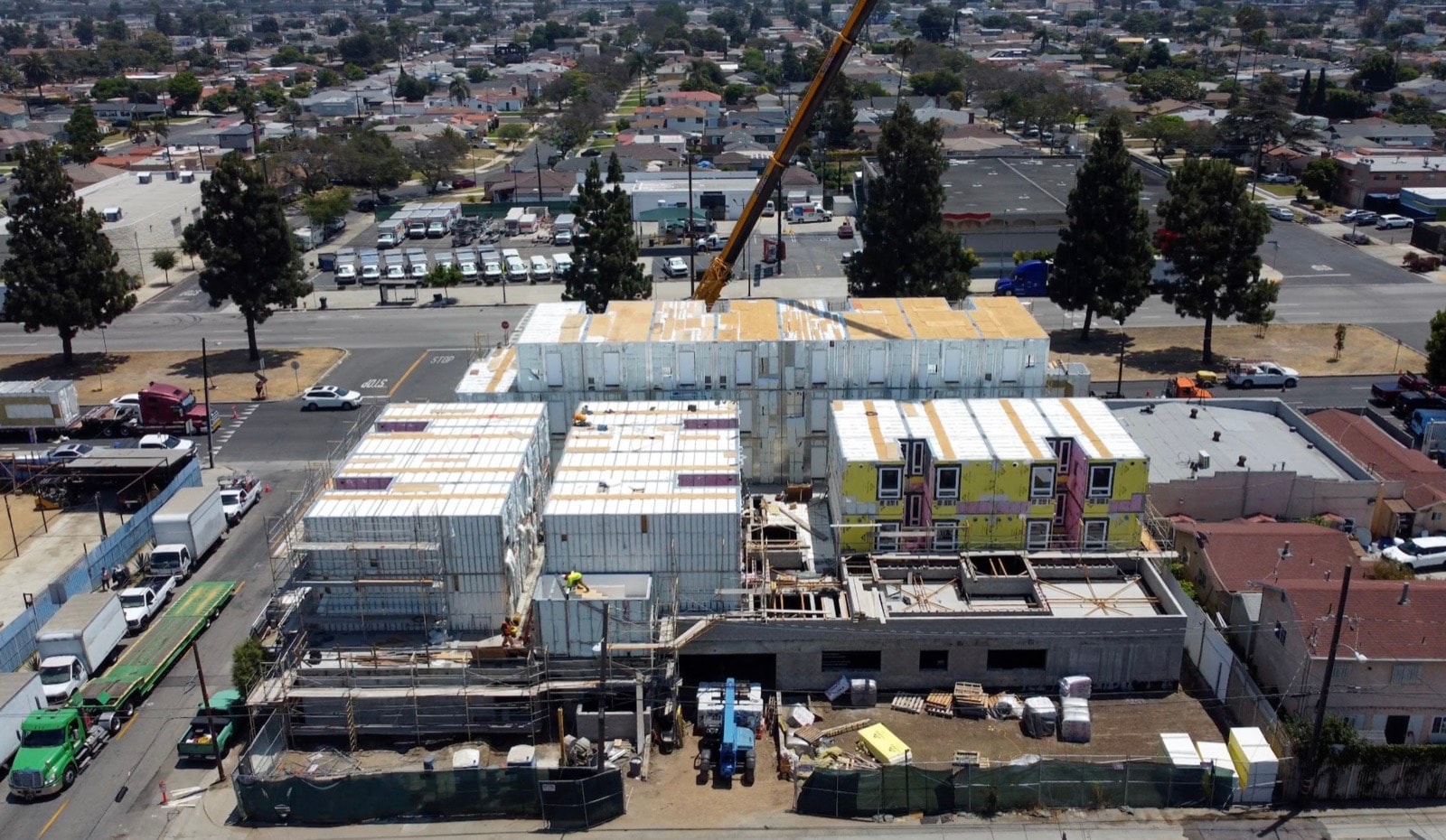 Aerial view of finished volumetric modules being set onto the building podium with a tower crane.