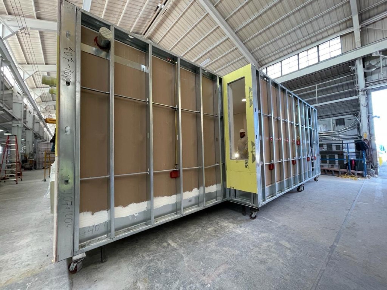 A volumetric module with yellow exterior sheathing and framed window and door openings.